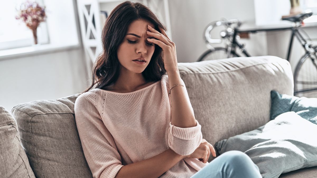 woman sitting on the couch holding her head due to fatigue after quitting alcohol